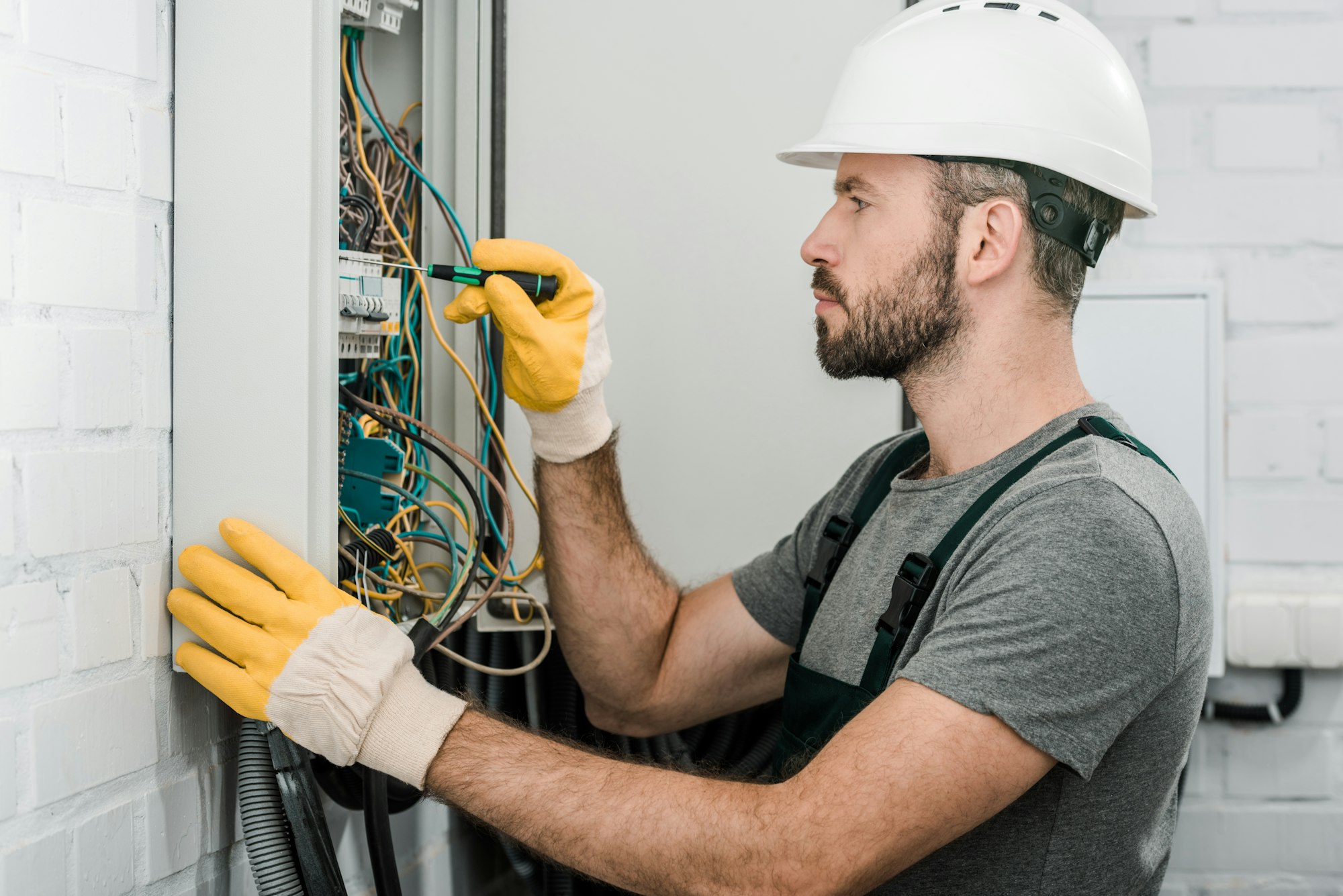 side-view-of-handsome-bearded-electrician-repairing-electrical-box-and-using-screwdriver-in-corridor.jpg